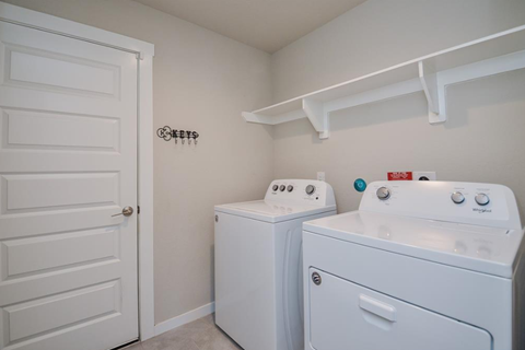 A white door is on the left of a wall with a clothesline and two washing machines.