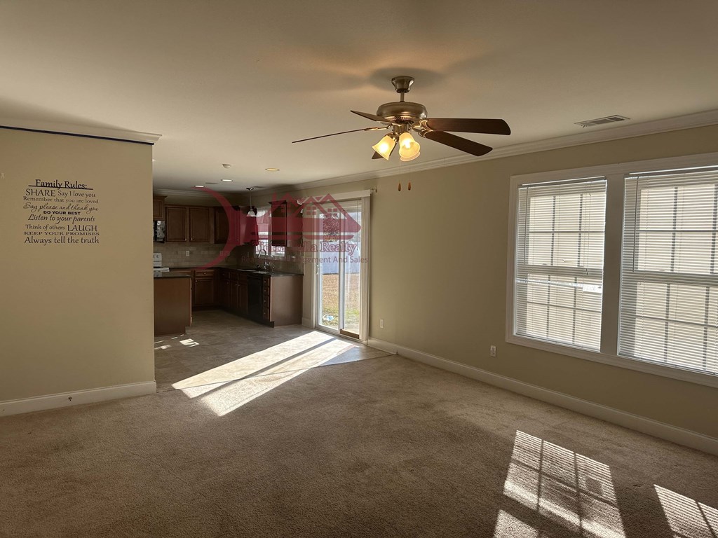 an empty living room with a ceiling fan and a kitchen