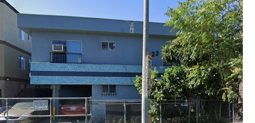 a blue apartment building with a fence and a tree