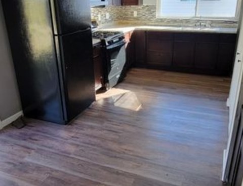 A black fridge in a kitchen with wooden flooring.