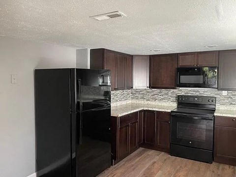 A black refrigerator and oven in a kitchen with brown cabinets.