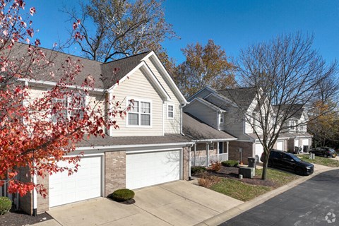 A house with a white garage door is surrounded by trees and a black car is parked in the driveway.