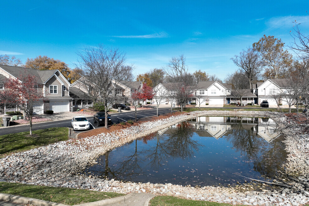 A residential street with houses on both sides and a pond in the foreground.