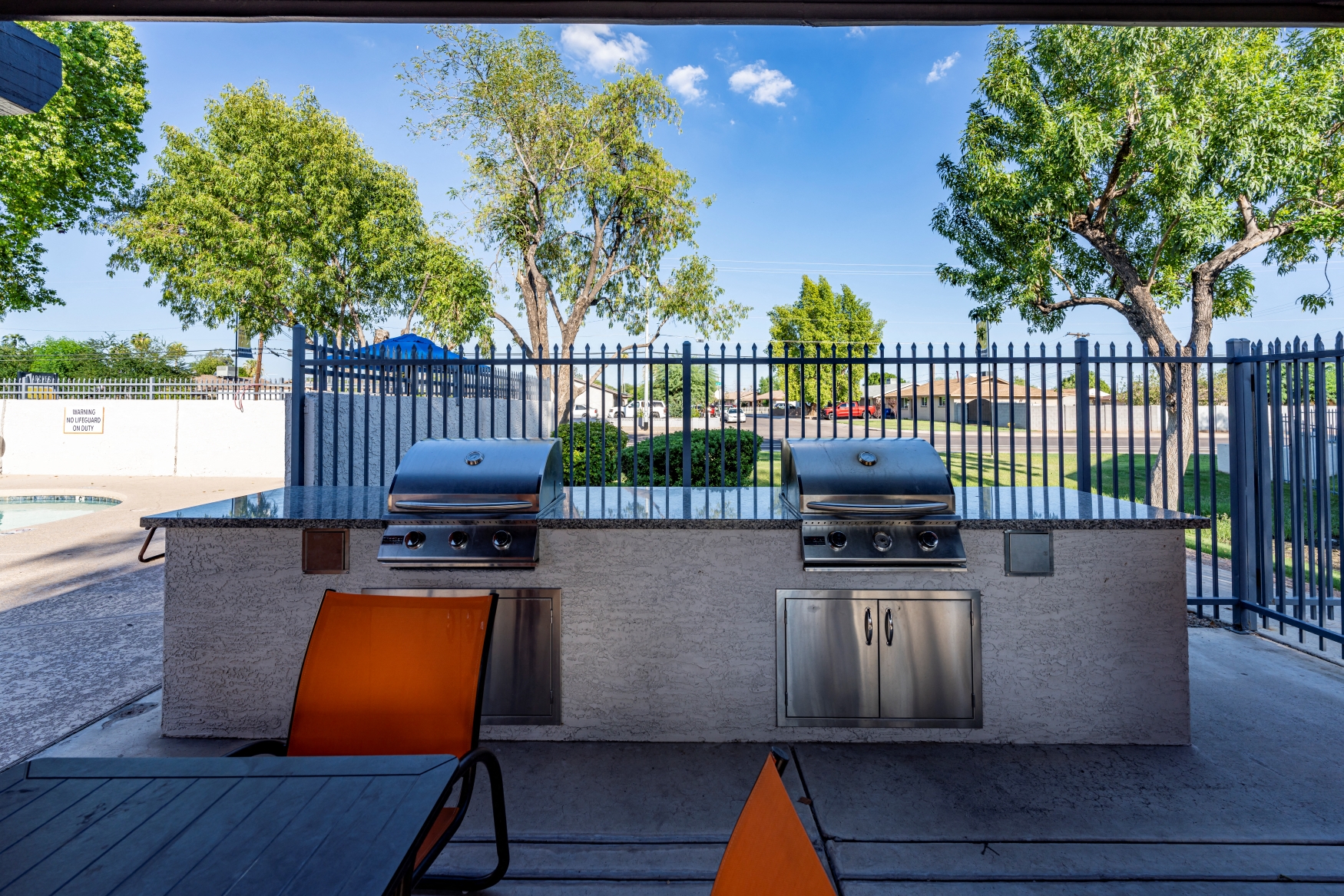 a patio with a barbecue grill and a table with orange chairs