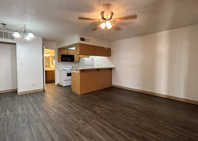 an empty living room with a kitchen and a ceiling fan