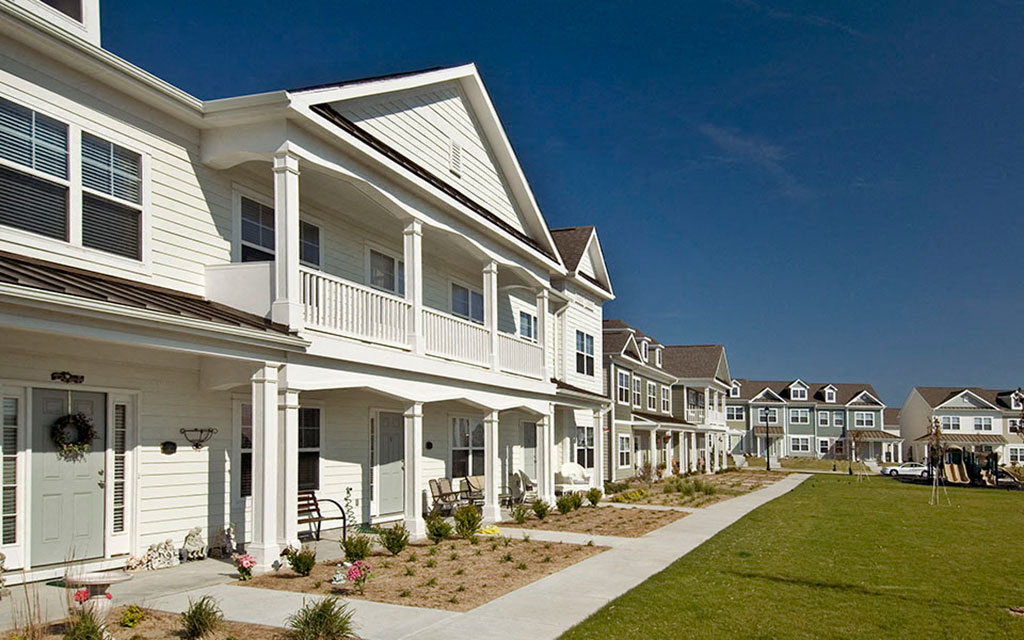 a row of white houses with a sidewalk and grass