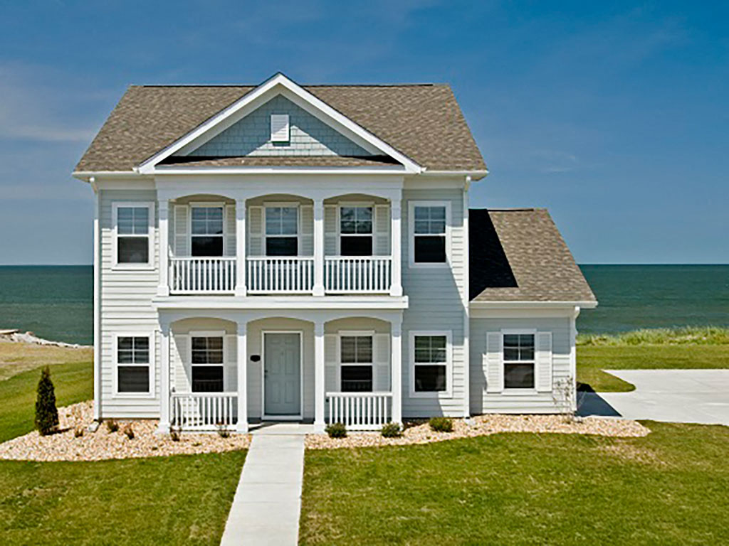a white house with a porch and the ocean in the background