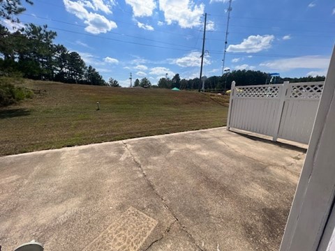 A concrete patio with a white fence and a grassy field in the background.