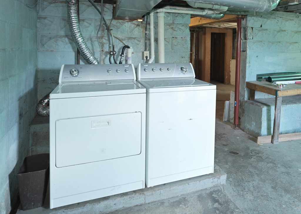 A white gas stove with an oven is in a room with a concrete floor and walls.