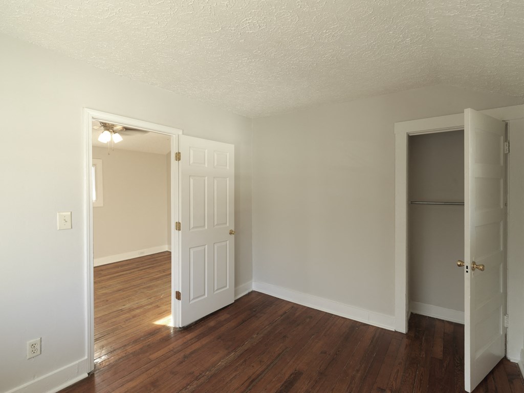 A room with white walls and wood floors, with two doors open.