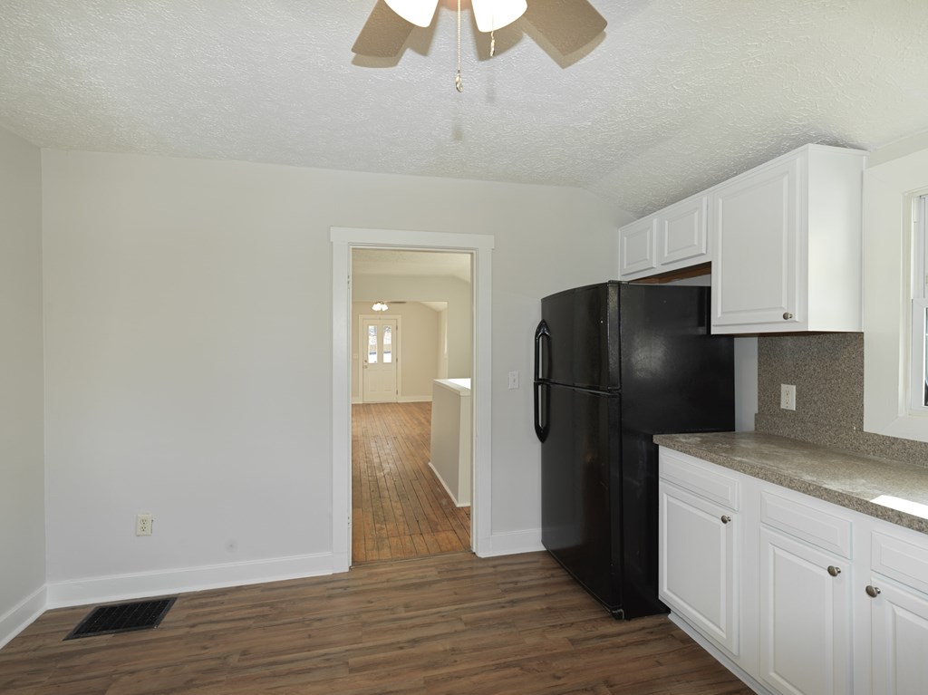 A black refrigerator in a kitchen with white cabinets.