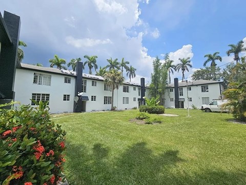 A white building with a green lawn in front and palm trees in the background.
