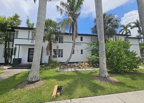 A white building with a black door and windows is surrounded by palm trees.