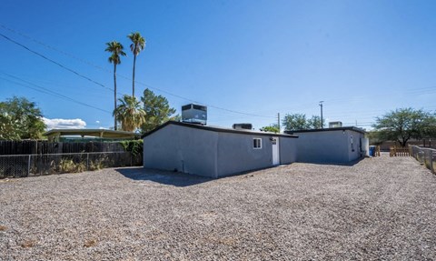 A gravel lot with a building and palm trees in the background.