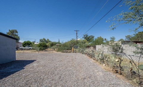 A gravel driveway leads to a house with a fence and vegetation on the side.