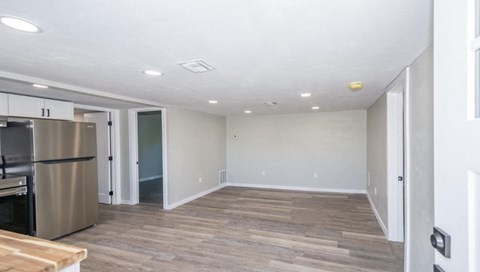 A kitchen with a refrigerator, wooden floors, and white walls.