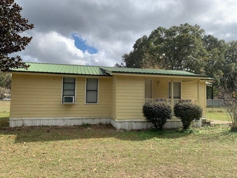 a yellow house with a green roof and some bushes