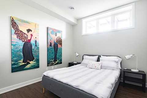 A bedroom with a bed, nightstand, and two paintings on the wall.