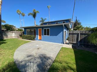 a blue house with a driveway and a yard with palm trees