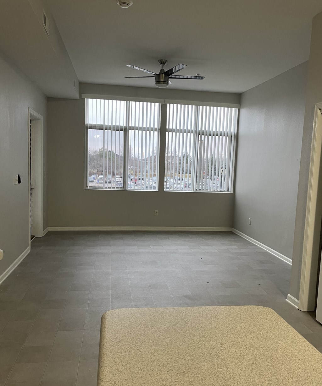 an empty living room with a ceiling fan and windows