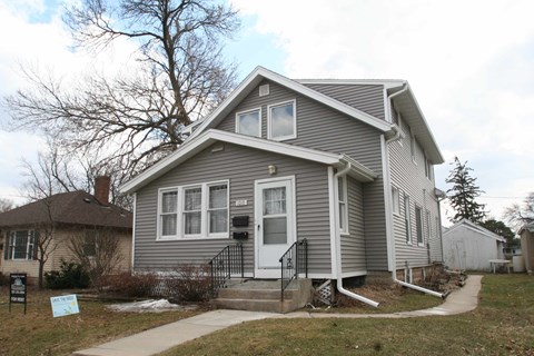 the front of a gray house with a yard and a sidewalk