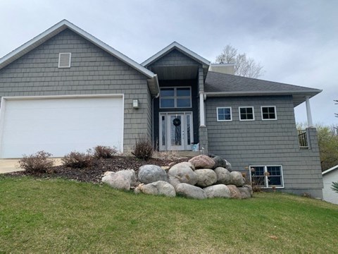 A grey house with a white garage door and a stone wall in front.