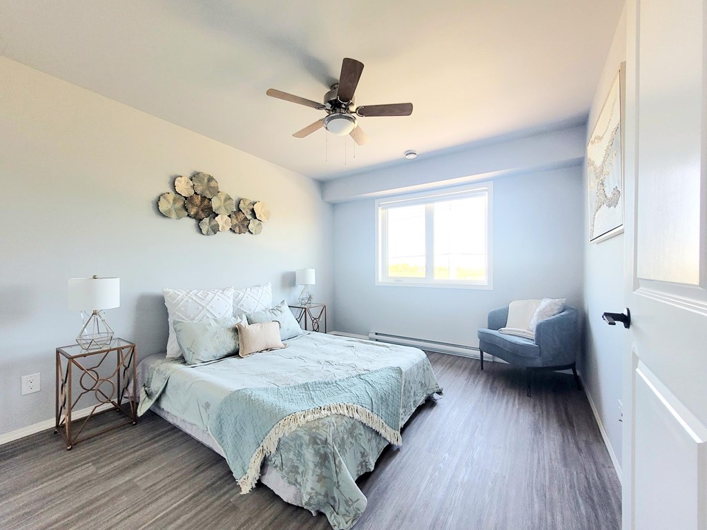 A bedroom with a bed, chair, and ceiling fan.