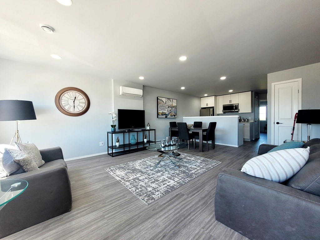 A living room with a grey couch, a coffee table, and a clock on the wall.