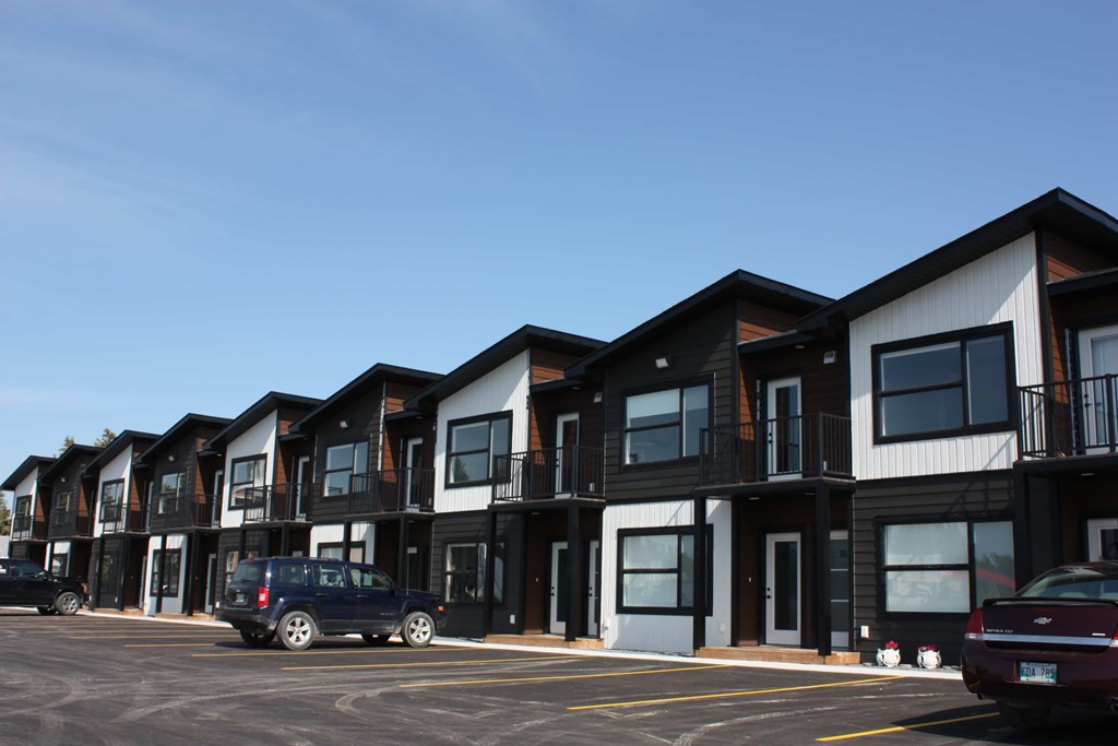 A line of modern townhouses with cars parked in front.