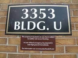 A sign on a brick wall that reads "3353 BLDG. U" and includes a warning about flood emergencies.