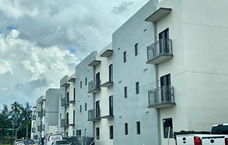 a white building with balconies and cars in front of a cloudy sky