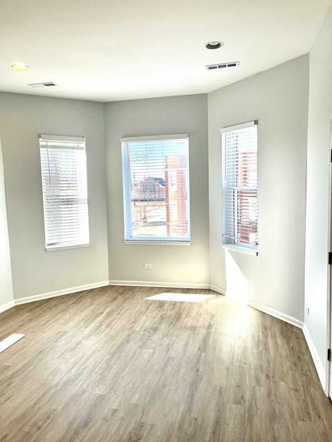 an empty living room with wood floors and three windows