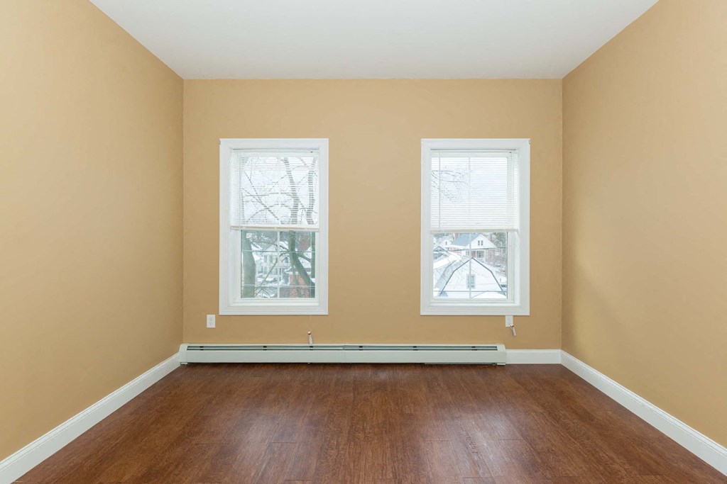 an empty room with wood floors and two windows