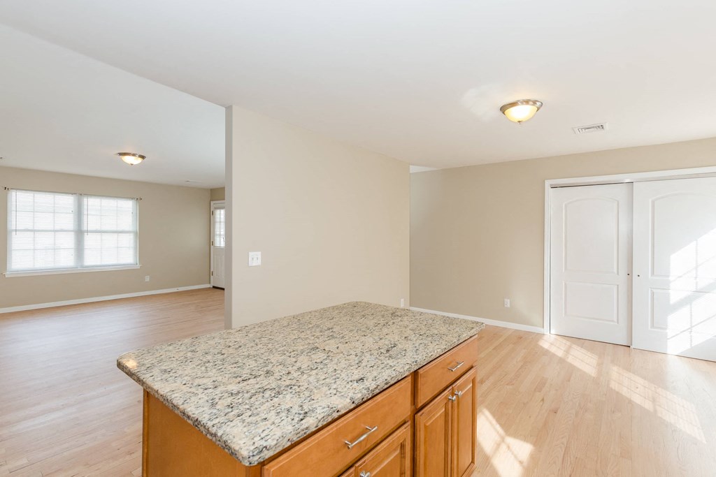 an empty kitchen with a granite counter top and a door to a living room