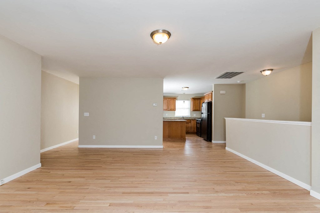 an empty living room with wood floors and a kitchen