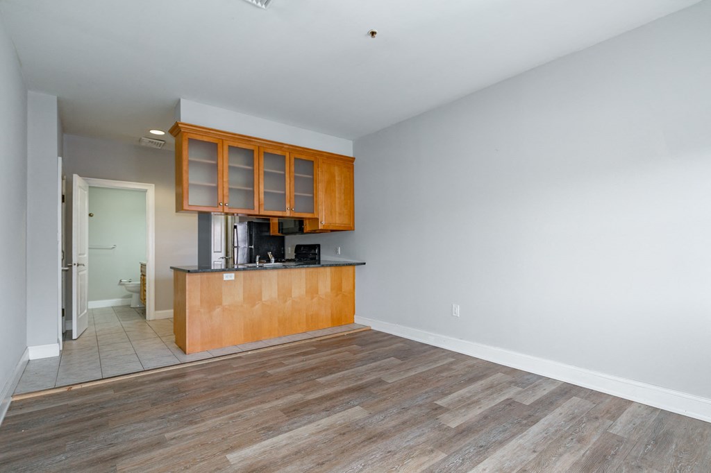 an empty living room with a kitchen and a door to a bathroom