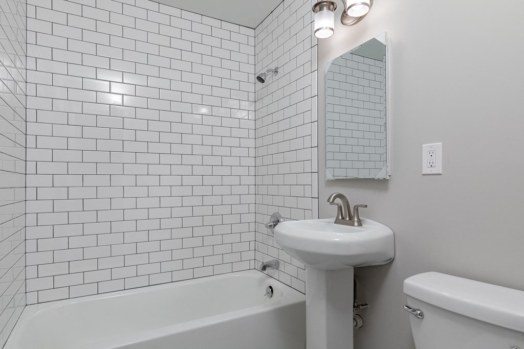 a white bathroom with white tiles and a sink and a bath tub
