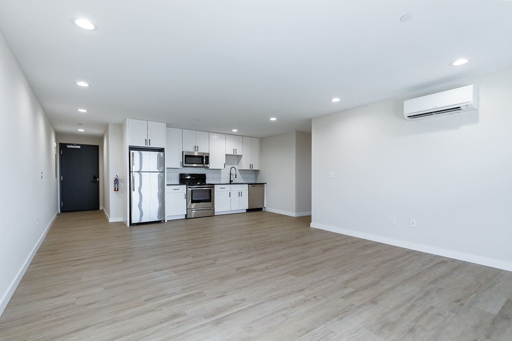 a living room and kitchen with white walls and wood floors