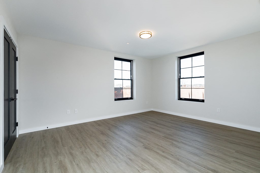 a living room with white walls and wood flooring and two windows