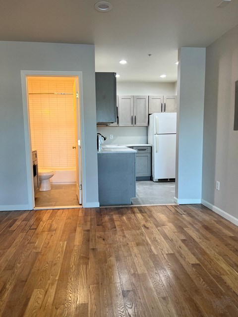 an empty living room with a kitchen and a door to a bathroom