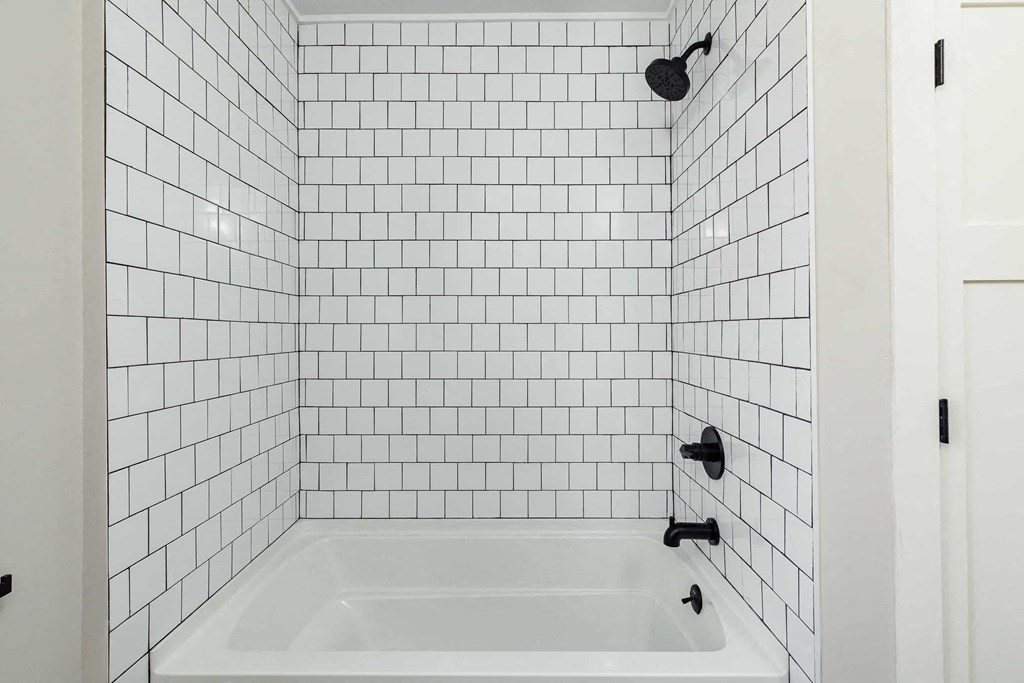 a white tiled bathroom with a white tub and a black shower