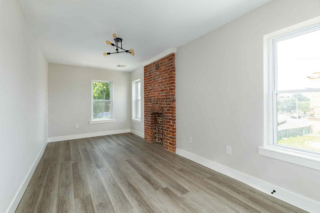 an empty living room with wood floors and a brick fireplace