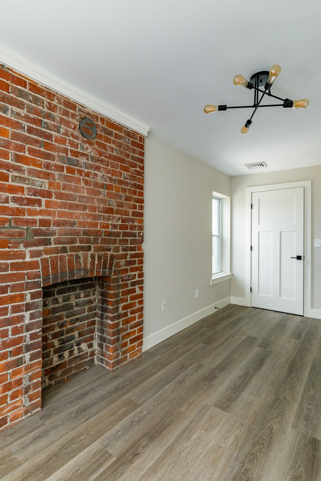 an empty living room with a brick fireplace and wooden floors