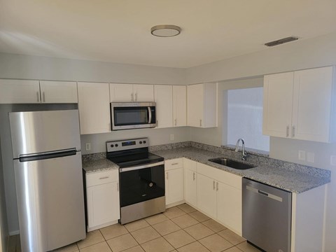 A kitchen with a refrigerator, microwave, oven, and sink.