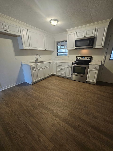 A kitchen with white cabinets and a wood floor.