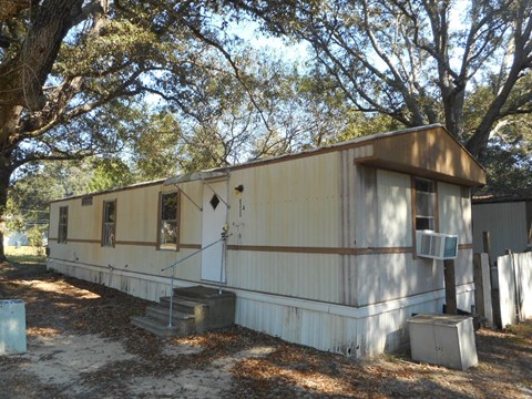 the exterior of a mobile home is shown with some trees