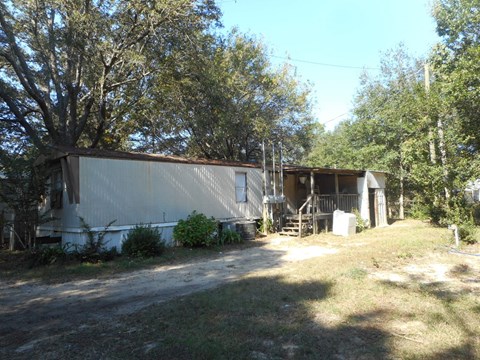a mobile home in a yard with trees and a driveway