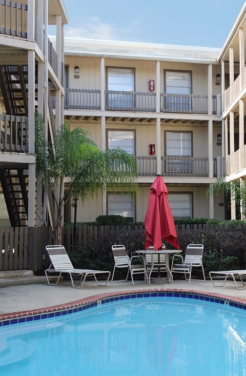 A pool with chairs and an umbrella in front of a building.