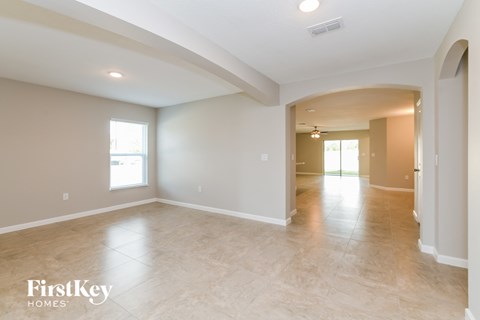 A spacious room with beige walls and flooring, and a large archway leading to another room.