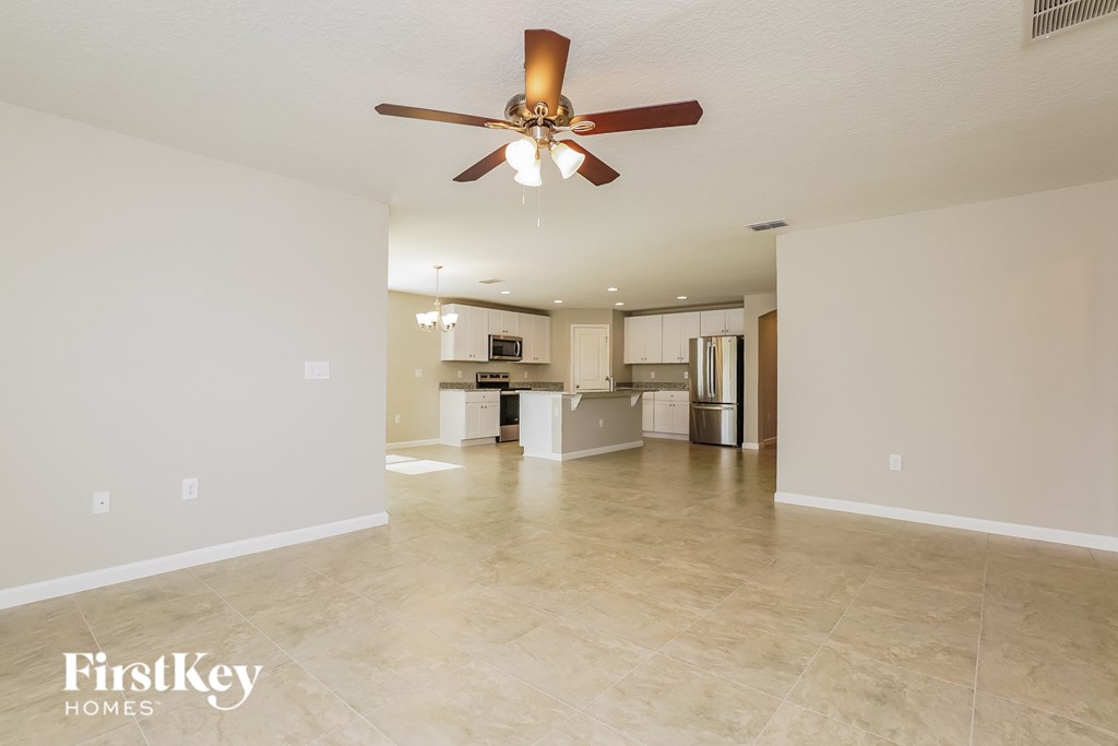 an empty living room with a ceiling fan and a kitchen